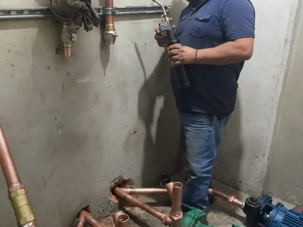 Plomero de AFA trabajando tubería de cobre junto a bombas de agua